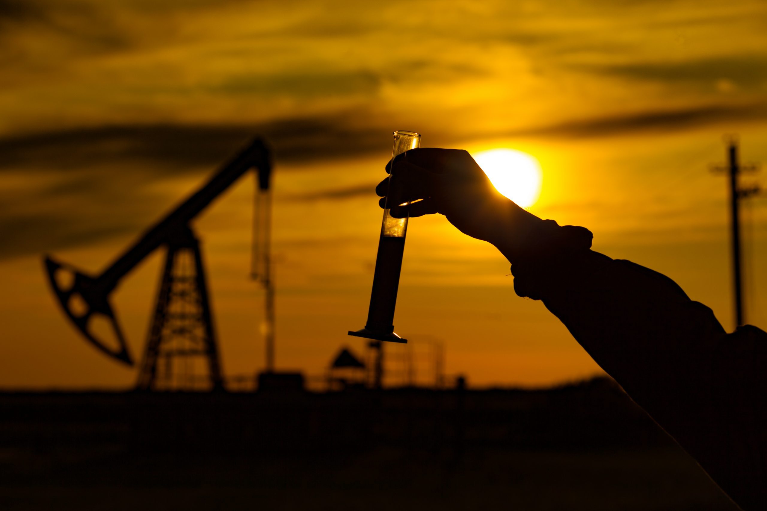 A man holding a flask of oil. Oil rigs in the background. Oil production in Russia. Sunset. Oil pumping